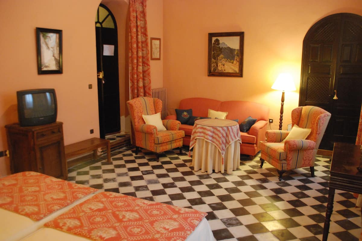 Habitación de hotel con piso a cuadros, un sofá, dos sillones, una mesita, un televisor y una lámpara.