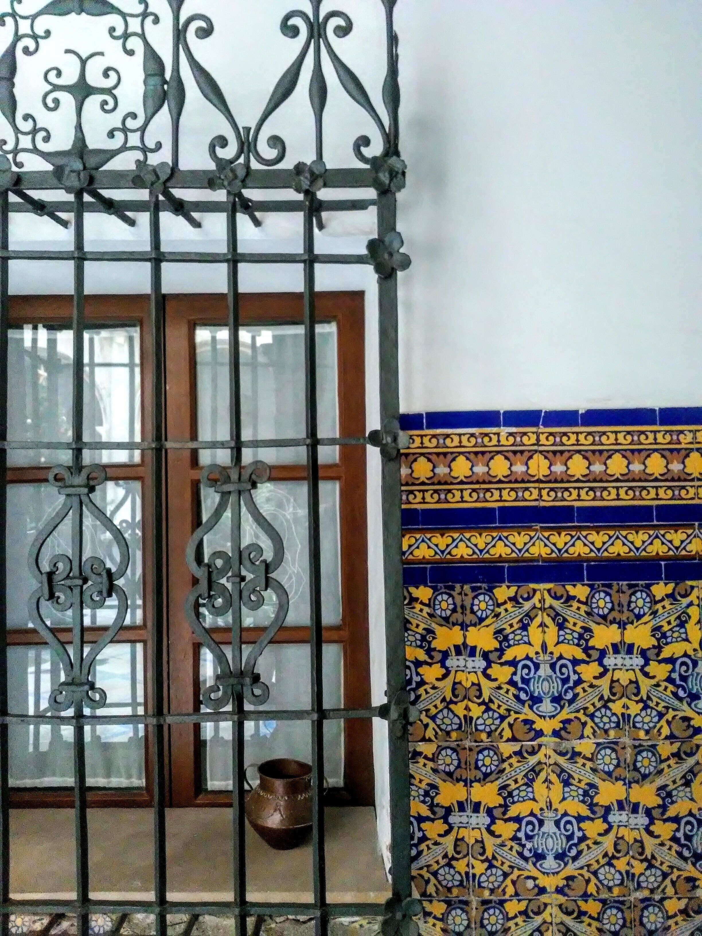 A metal gate with intricate designs, a window with frosted glass, and a wall with patterned tiles.