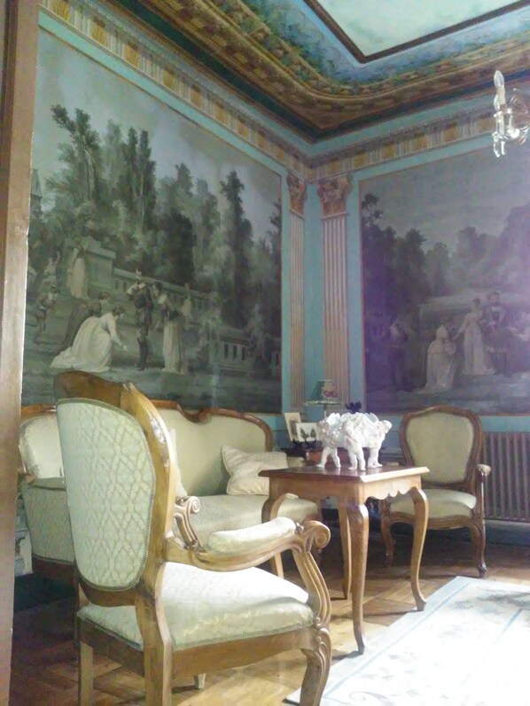 Una habitación de diseño clásico, con un gran mural en la pared, un sofá de madera, una pequeña mesa y una silla.