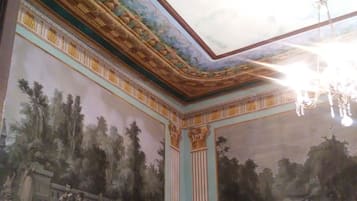 Una habitación con un mural, techo ornamentado y muebles clásicos.