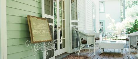 A porch with wicker furniture, a white bench, and a sign that reads "He has made everything beautiful."