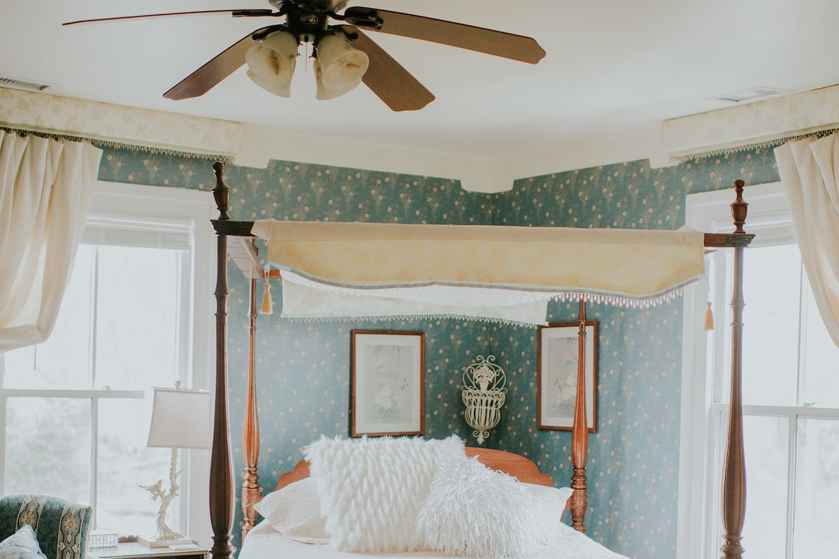 A four-poster bed with a canopy, a wooden bench, a nightstand with a lamp, and a chair with a cushion.