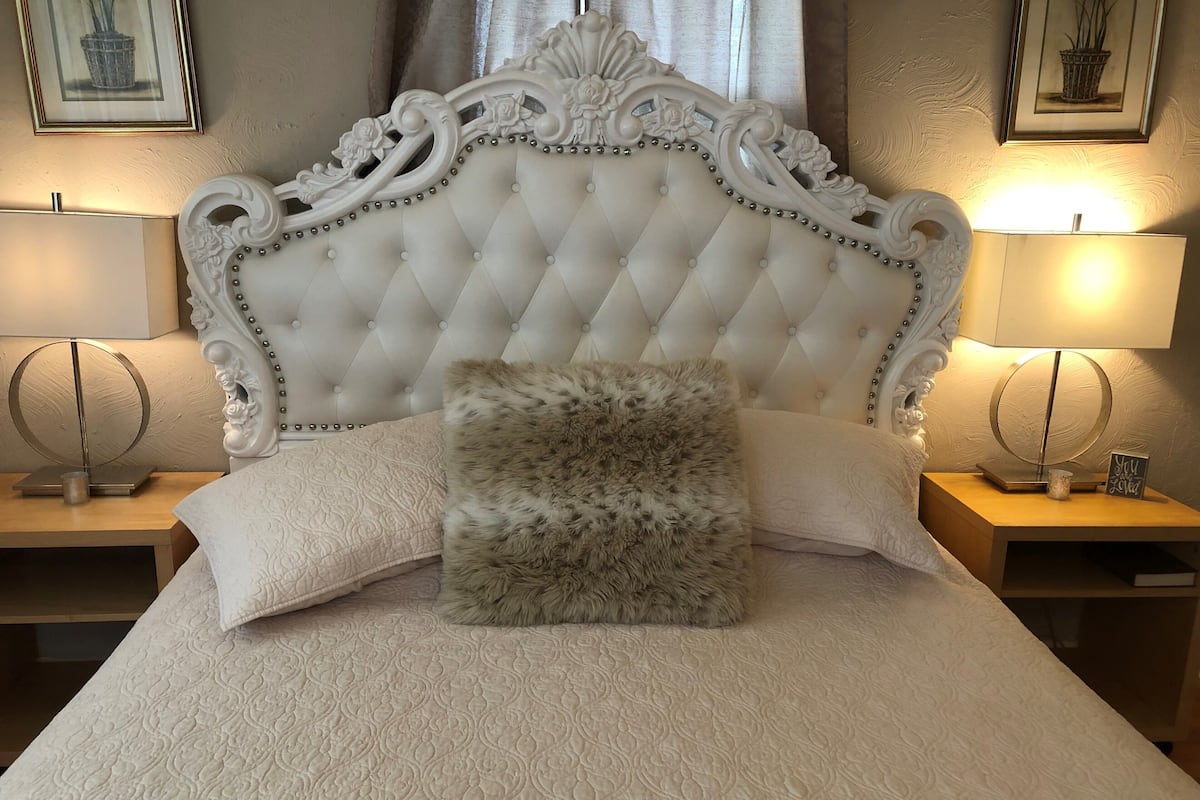 A bed with a tufted headboard, two bedside tables, and a fluffy pillow.