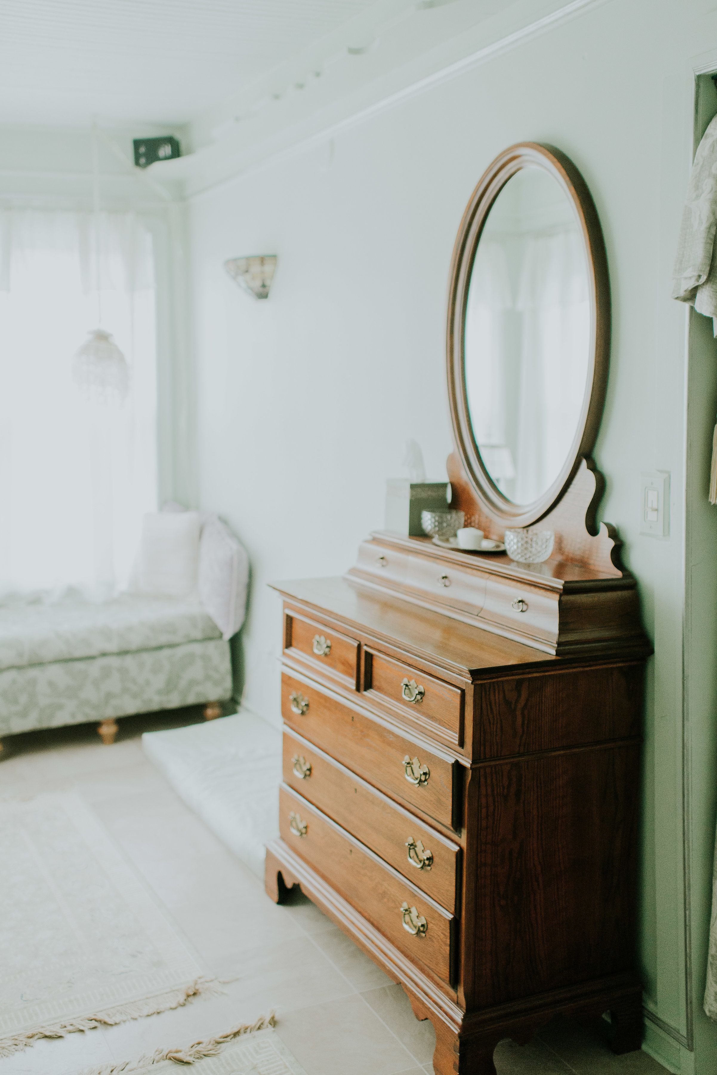 A bedroom with a wooden dresser, a mirror, and a bed with a white bedspread.