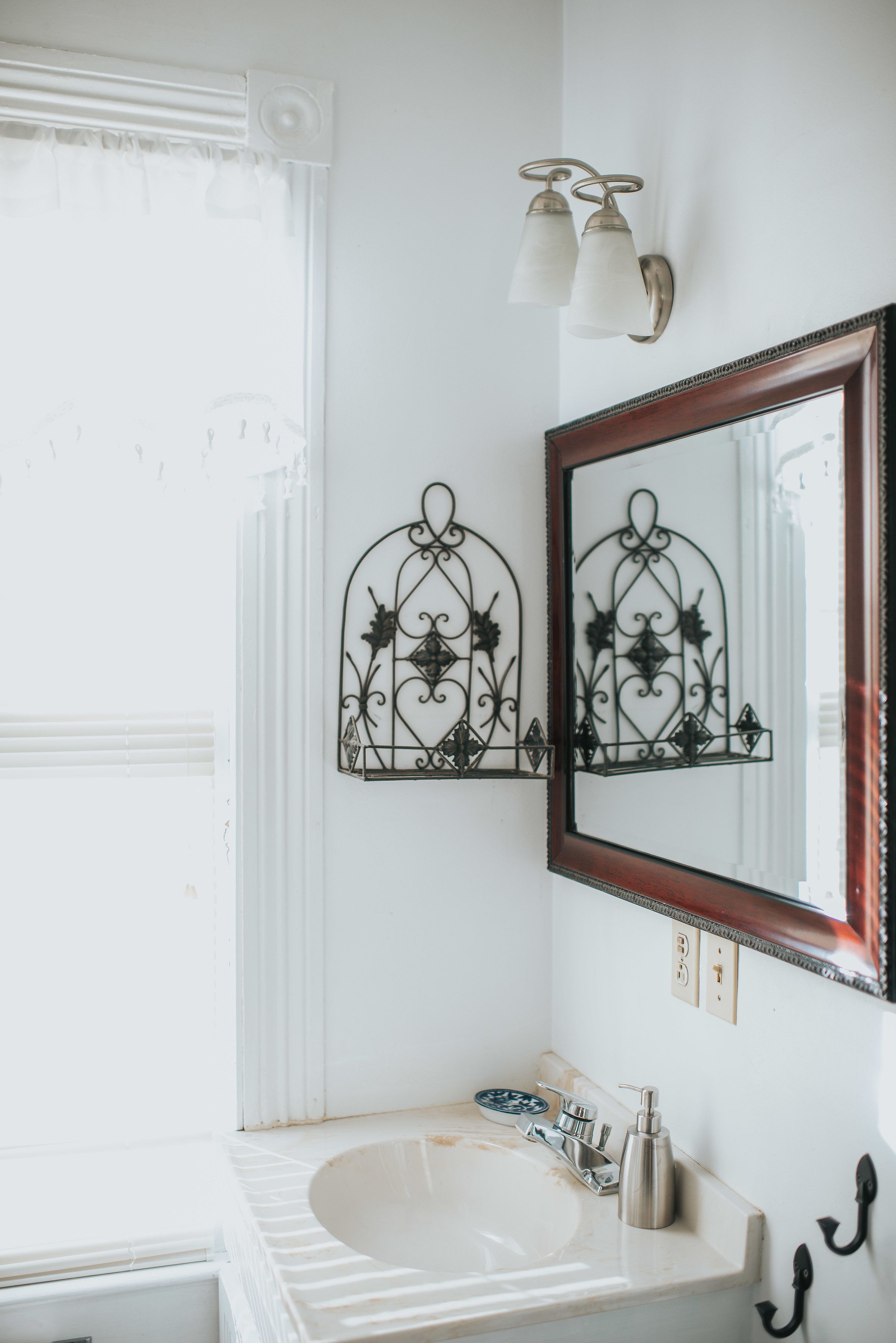 A bathroom with a white sink, a mirror with a decorative frame, and wall-mounted sconces.