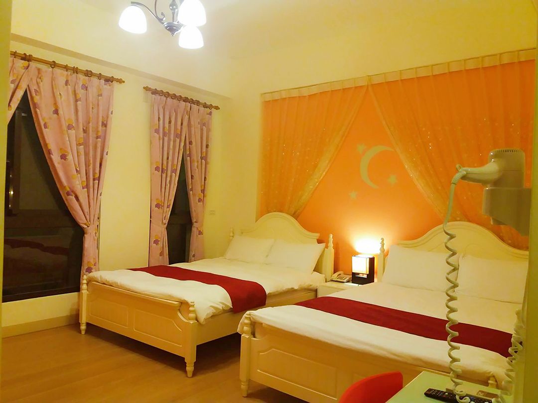 Een hotelkamer met twee bedden, een nachtkastje met een lamp en een raam met gordijnen.