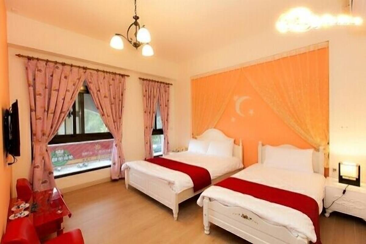 Une chambre d’hôtel avec deux lits, une table rouge et une fenêtre avec des rideaux.