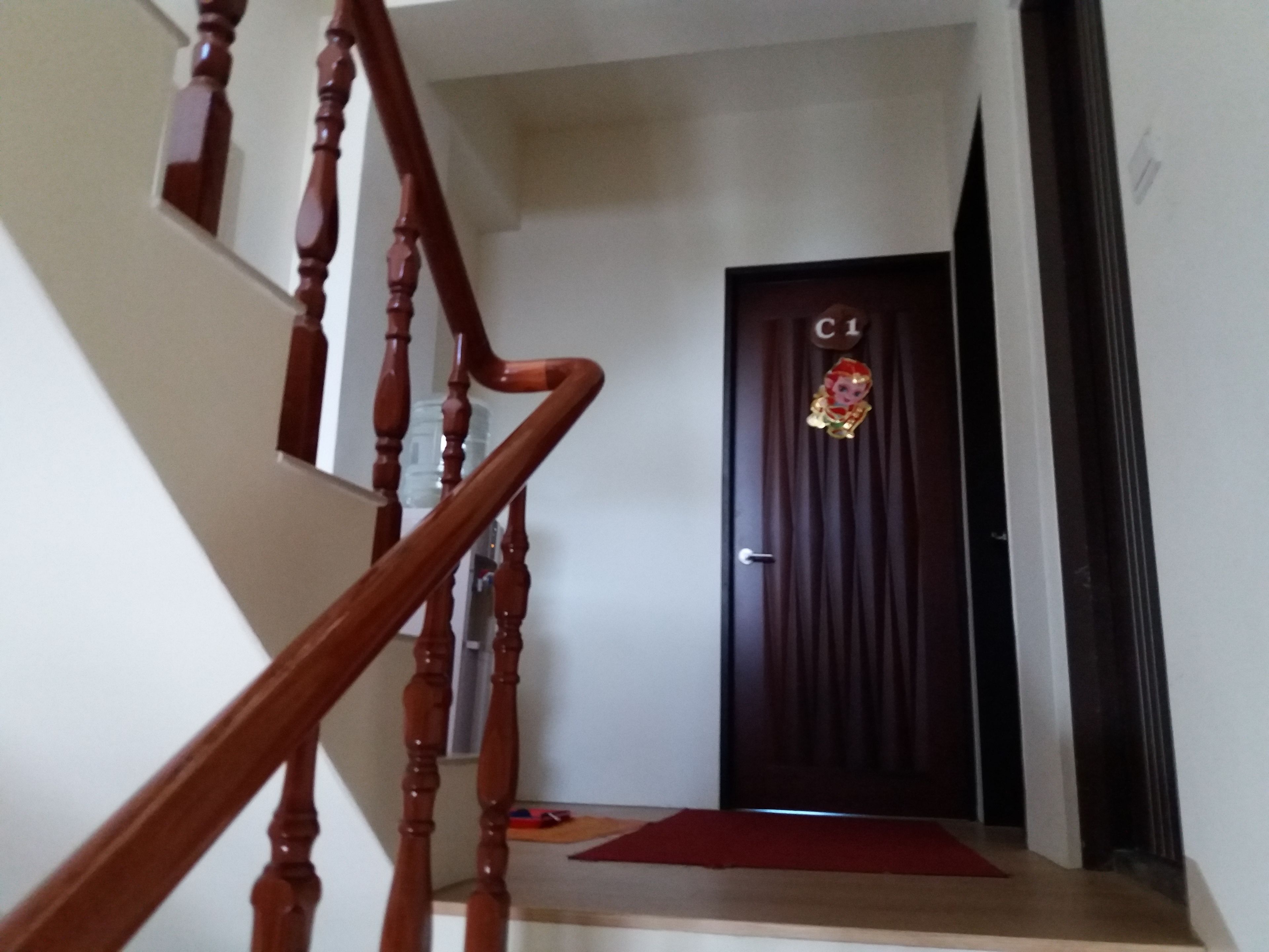 A wooden staircase leading to a dark door with a small red mat at the bottom.