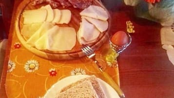 Una mesa con un plato de pan rebanado, un plato de queso y un plato de carne. Hay un farol y un jarrón con flores sobre la mesa.