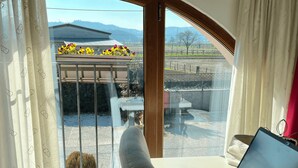 A room with a laptop on a table, a chair, and a view of a garden and mountains through a large window. - Country Home B&B Il Melo (Vicenza)