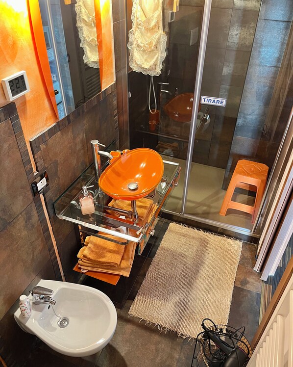 A bathroom with a glass-enclosed shower, a white sink, and a glass vessel sink with a towel rack. - Country Home B&B Il Melo (Vicenza)