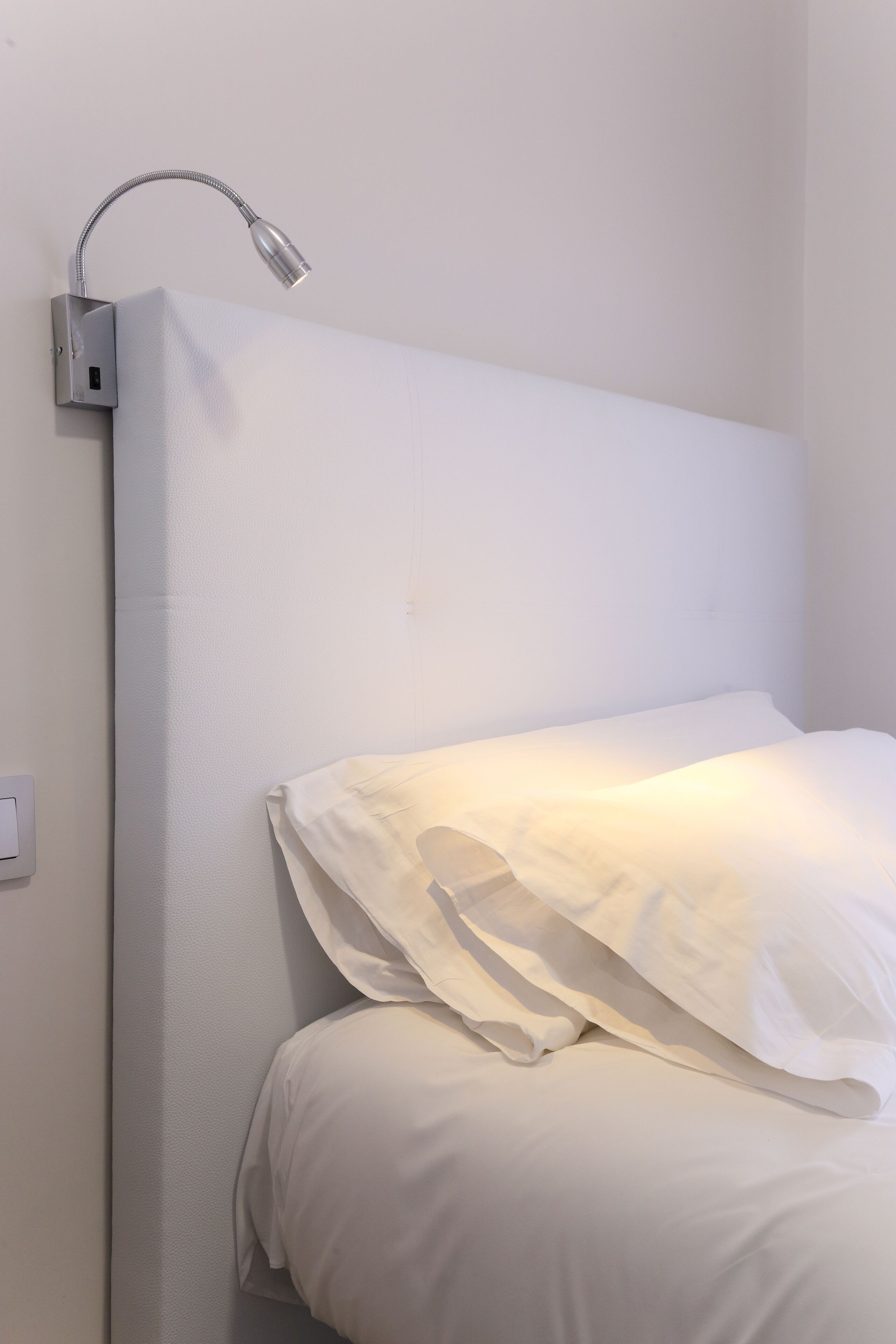 Ein Bett mit weißer Bettwäsche und einer Wandleuchte.