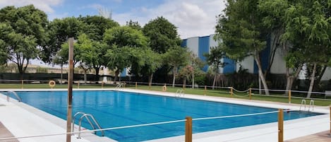 A rectangular swimming pool with a wooden deck surrounding it, metal railings, and trees in the background.