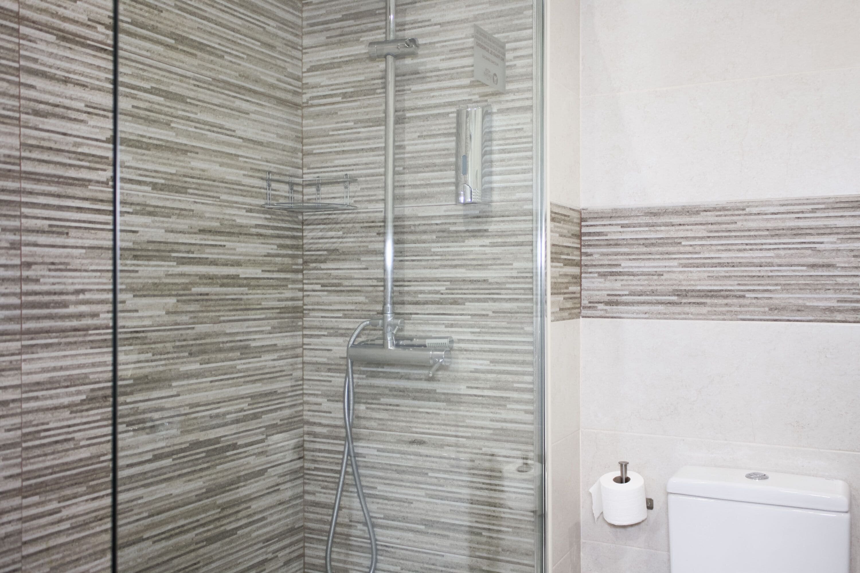 Ein Badezimmer mit Duschkabine aus Glas, Toilette und Handtuchhalter.