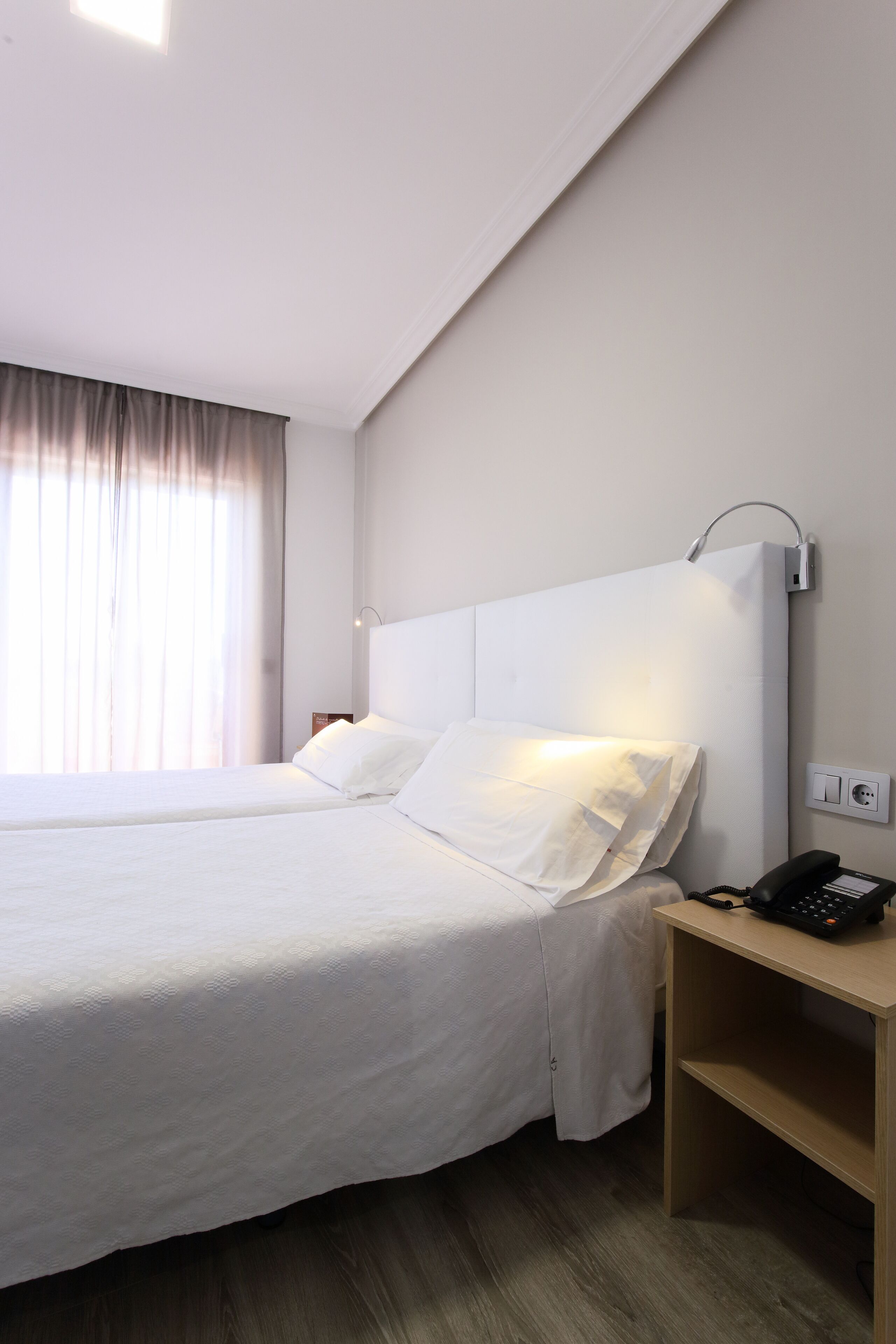 Habitación de hotel con una cama grande, una mesita de noche con un teléfono y una lámpara de pared.