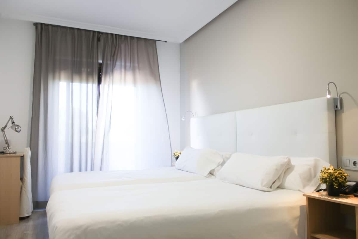 A modern hotel room with a large bed, a bedside table, a lamp, and a nightstand with a phone and a plant.