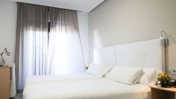 Una habitación de hotel moderna con una cama grande, una mesita de noche, una lámpara y un atril con un teléfono y una planta.