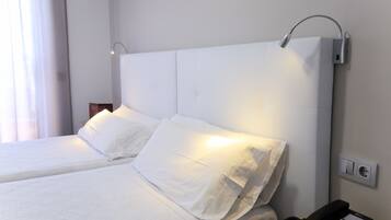 Ein Hotelzimmer mit Bett, weißer Bettwäsche, einem Nachttischtelefon und einer Wandleuchte.