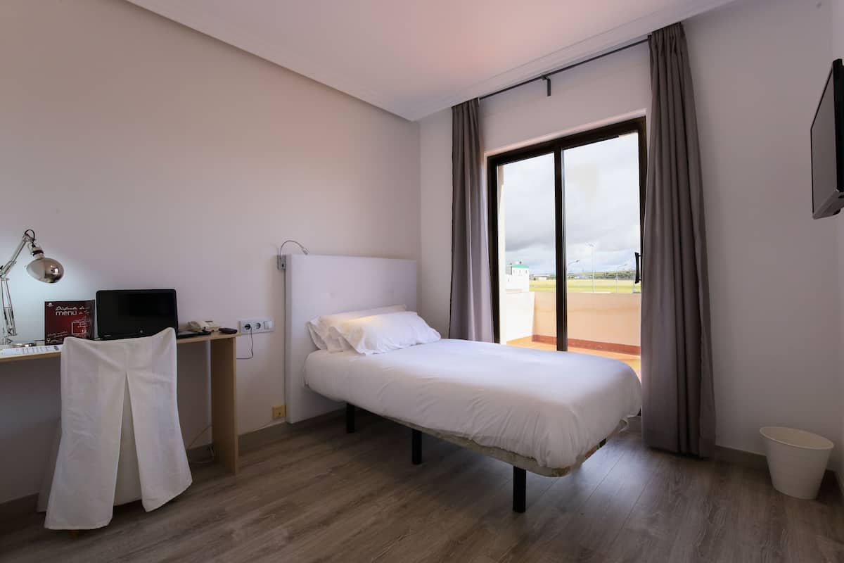 A hotel room with a bed, a desk with a computer, a chair, and a window with curtains.
