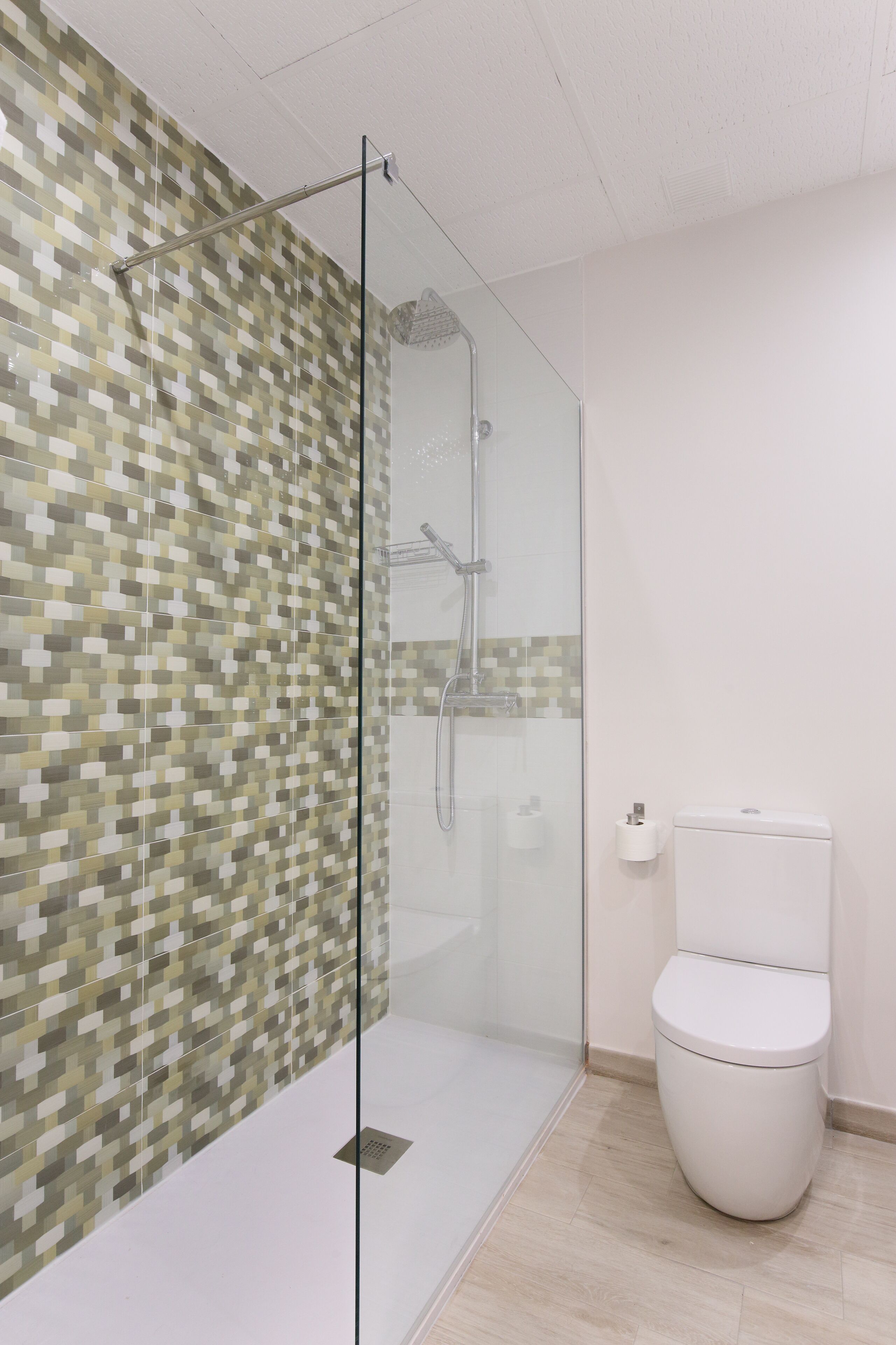 Un baño con cabina de ducha de vidrio, inodoro y pared con azulejos.