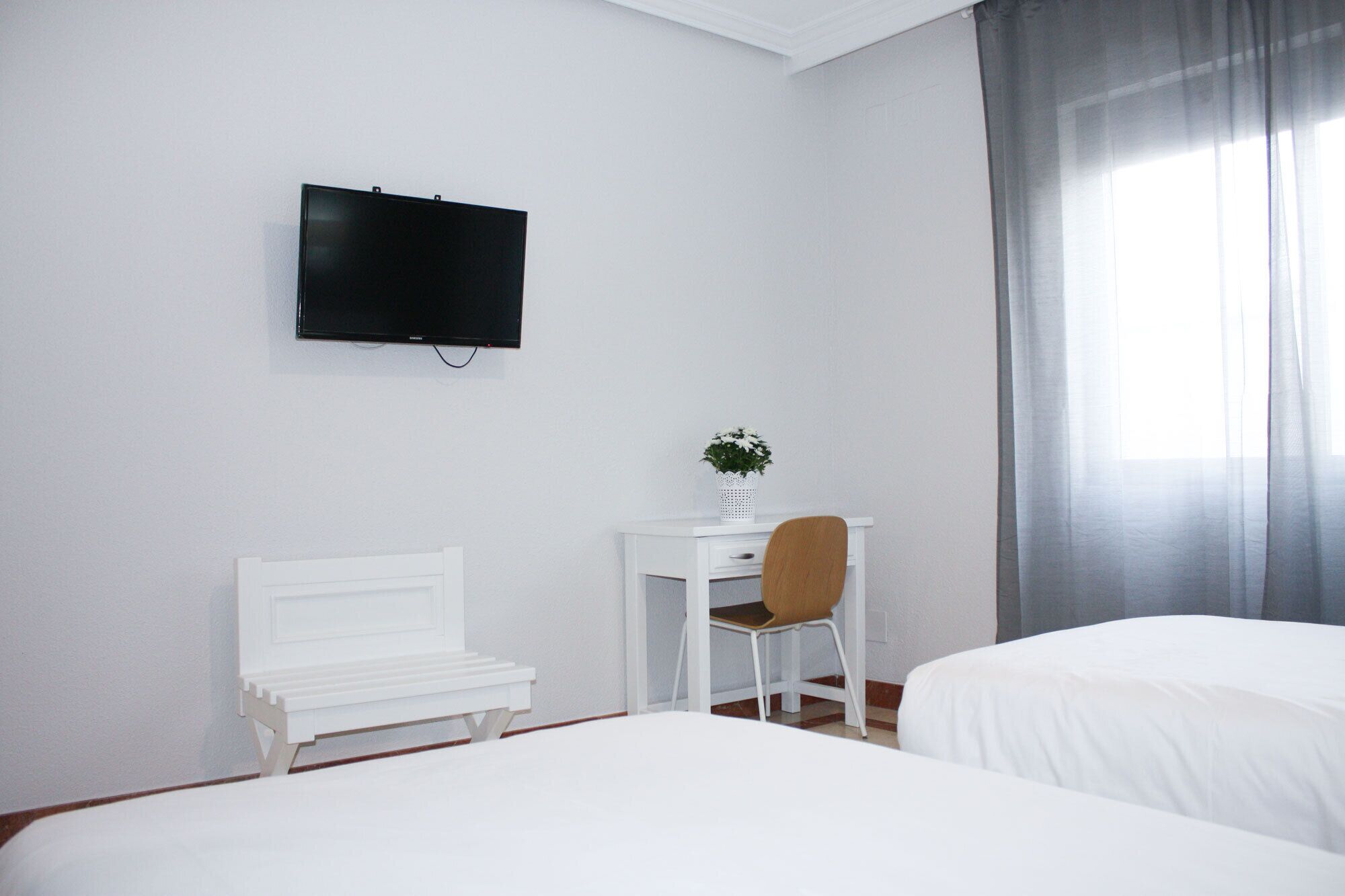 A hotel room with a bed, a desk with a chair, a television on the wall, and a window with curtains.