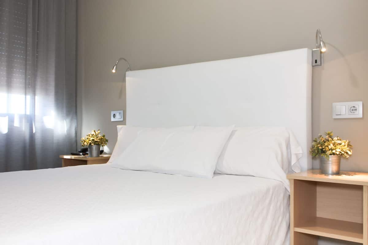 A neatly made bed with white linens, two bedside tables with lamps, and a potted plant on each.