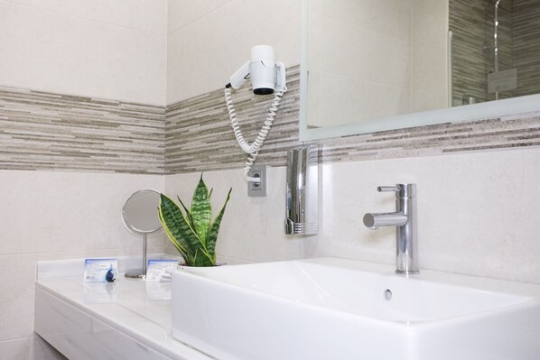 A bathroom with a white sink, a handheld hair dryer, a mirror, and a potted plant. - Hotel Castilla Torrijos (Torrijos)