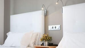 A modern hotel room with two beds, a bedside table with a plant, and a wall-mounted light fixture. - Hotel Castilla Torrijos (Torrijos)