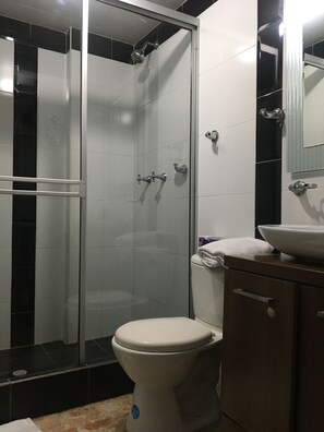 A bathroom with a glass-enclosed shower, a white toilet, and a sink with a mirror above it. - Hotel Ejecutivo Av Esperanza (Bogotá)