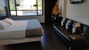 A modern bedroom with a large bed, a black leather sofa, a TV mounted on the wall, and a window with a view of the outside. - Hotel Ejecutivo Av Esperanza (Bogotá)