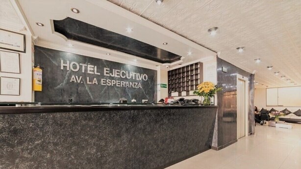 A hotel reception area with a marble counter, framed certificates, and a wall-mounted shelf with books. - Hotel Ejecutivo Av Esperanza (Bogotá)