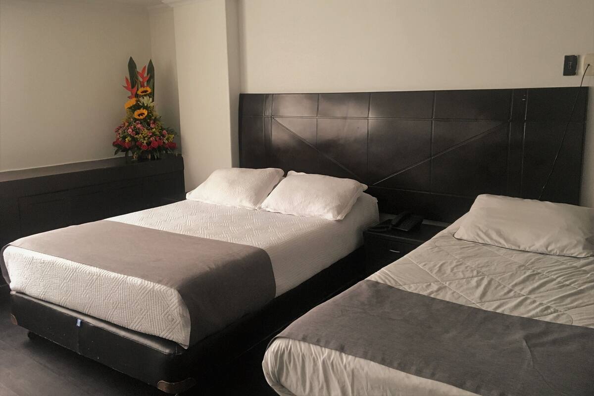 A hotel room with two beds, a dark headboard, and a floral arrangement on the wall.