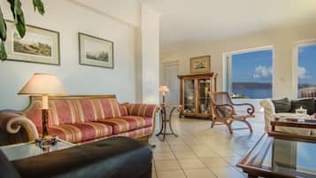Un salon avec un canapé rouge, un fauteuil noir, un meuble en bois et une vue sur la mer par une grande fenêtre.
