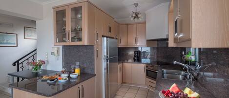 A modern kitchen with wooden cabinets, a stainless steel refrigerator, a coffee maker, and a fruit bowl on the counter.