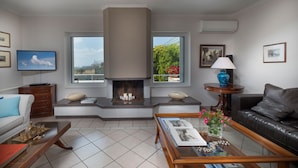A living room with a fireplace, a sofa, a coffee table, and a TV. - Sounio Villa (Lavreotiki)