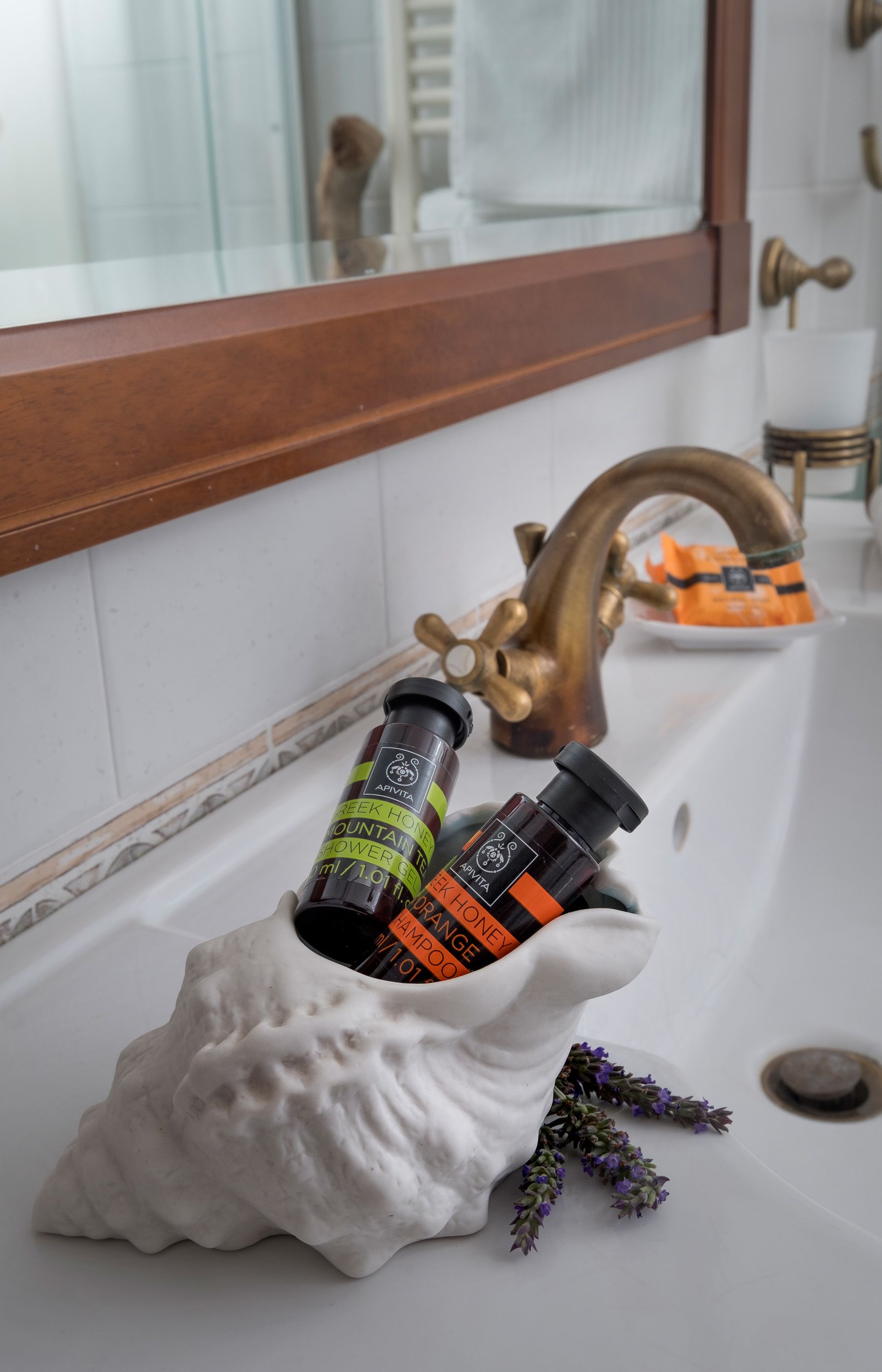 A bathroom sink with a white ceramic shell holding two bottles of shampoo and conditioner, a brass faucet, and a mirror above.