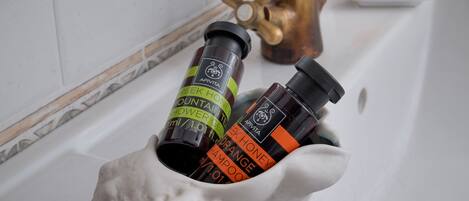 A bathroom sink with a white ceramic shell holding two bottles of shampoo and conditioner, a brass faucet, and a mirror above.