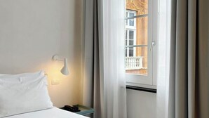 Ein Hotelzimmer mit Bett, Nachttisch, Lampe und einem Fenster mit Vorhängen.