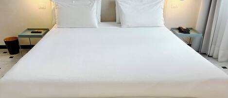 A large bed with white linens, two bedside tables with lamps, and a padded headboard.