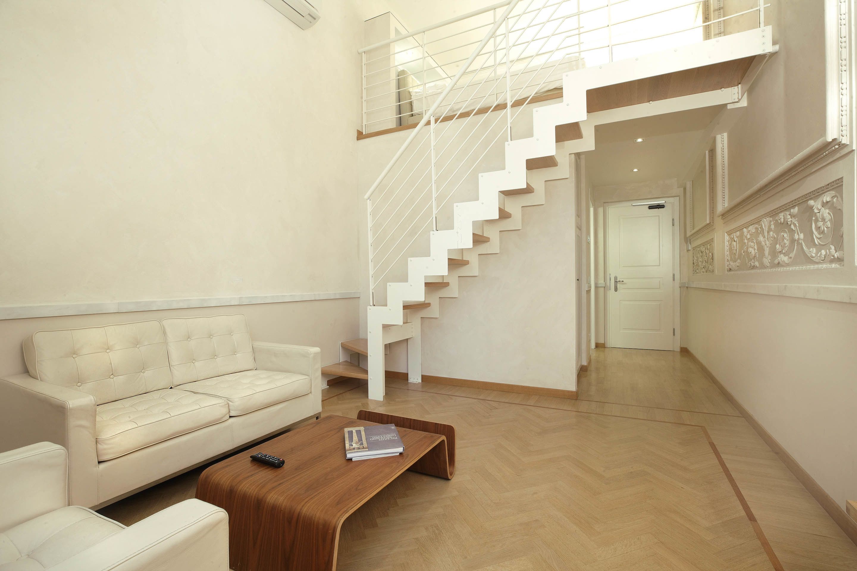 Una sala de estar moderna con una escalera blanca, un sofá y una mesa de centro.