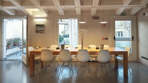 Ein Konferenzraum mit einem langen Tisch, weißen Stühlen, Pendelleuchten und Blick durch die Tür.