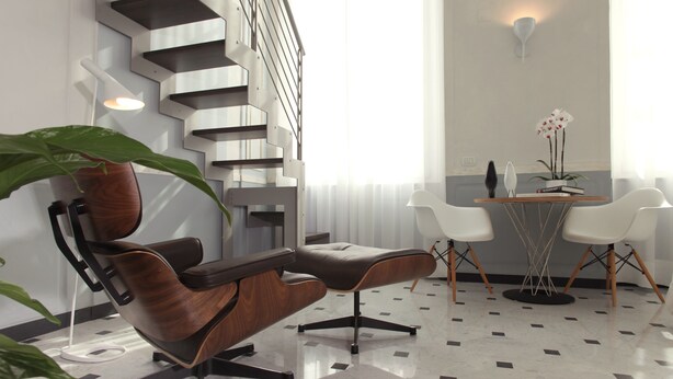 Ein modernes Interieur mit Treppe, braunem Ledersessel, weißem Tisch mit Stühlen und einer Topfpflanze.