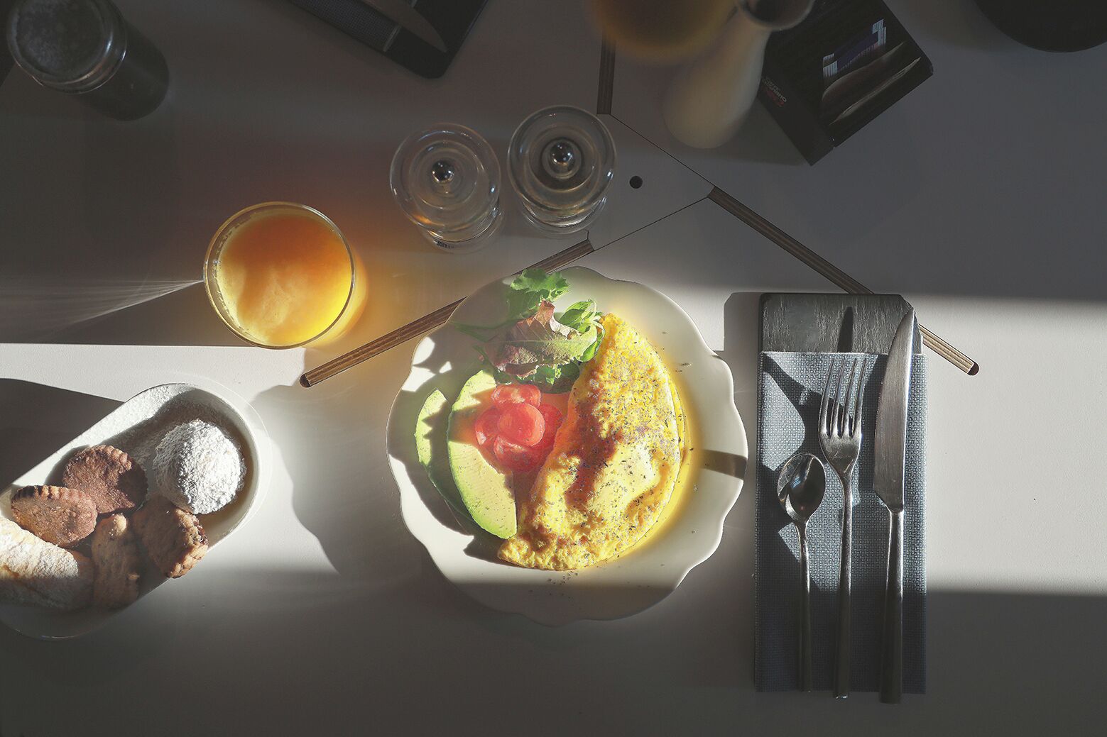 A breakfast setting with a plate of food, a glass of orange juice, and a napkin with cutlery.