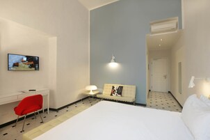 A hotel room with a bed, a desk, a chair, a TV, a sofa, and a lamp.