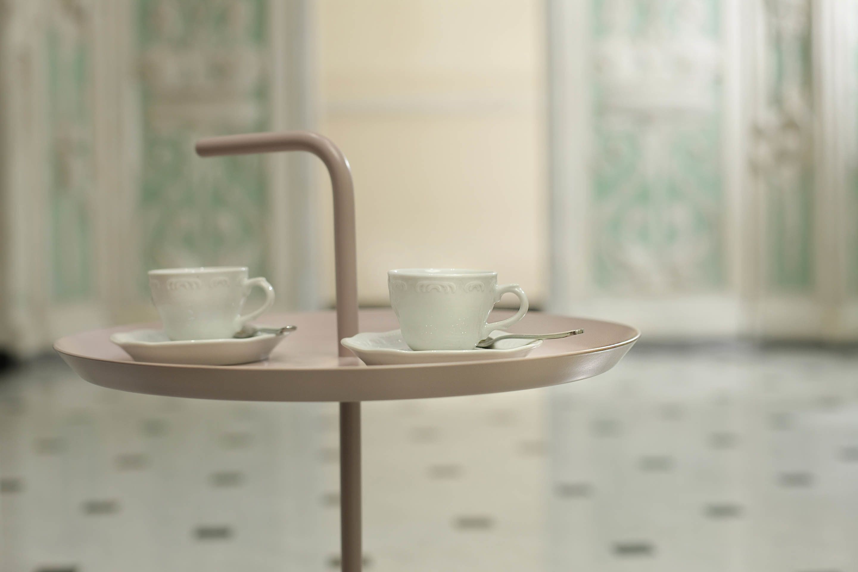 Une petite table avec deux tasses blanches et une cuillère sur un plateau rose.