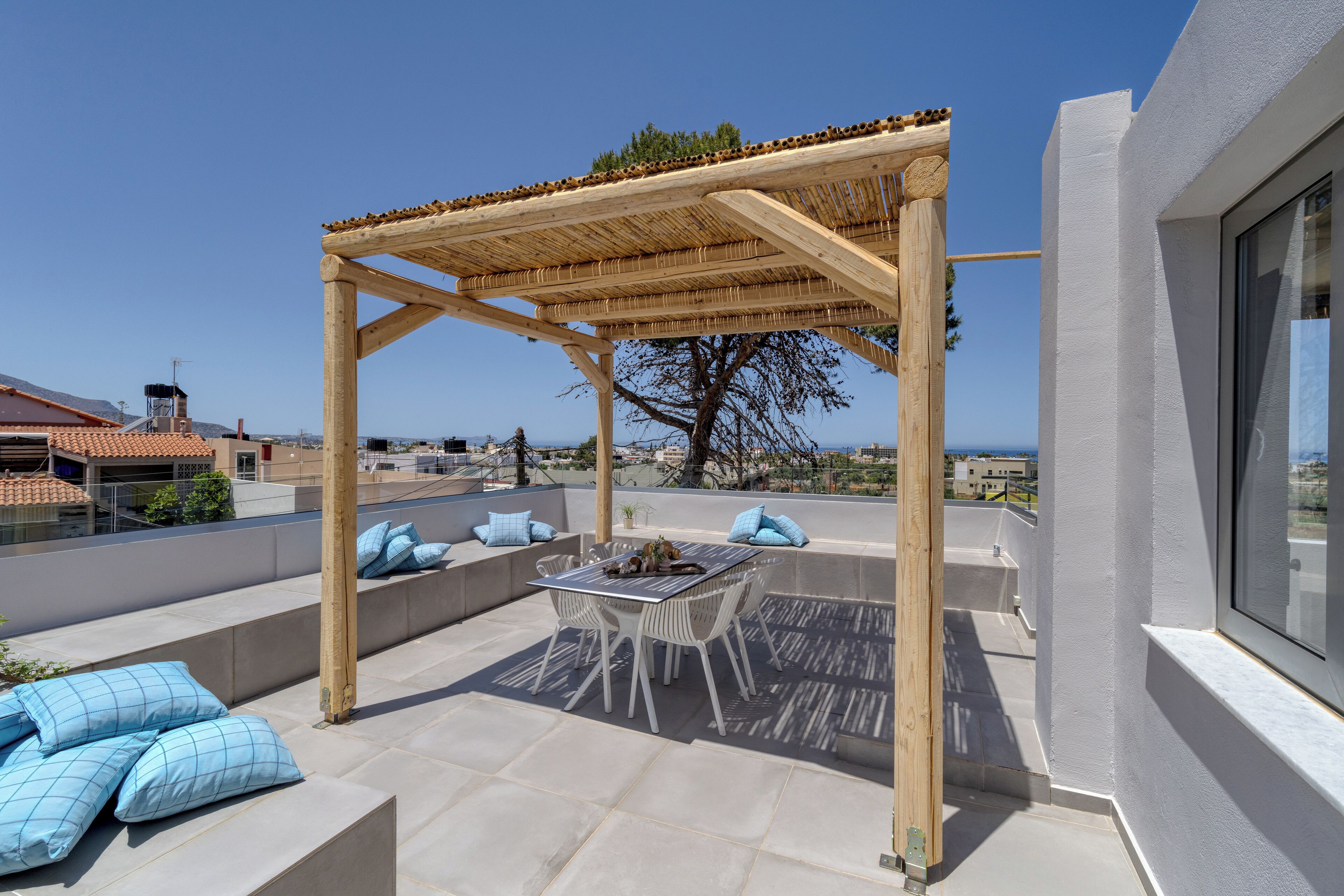 Eine Dachterrasse mit einer Pergola, Sitzgelegenheiten im Freien und Blick aufs Meer.