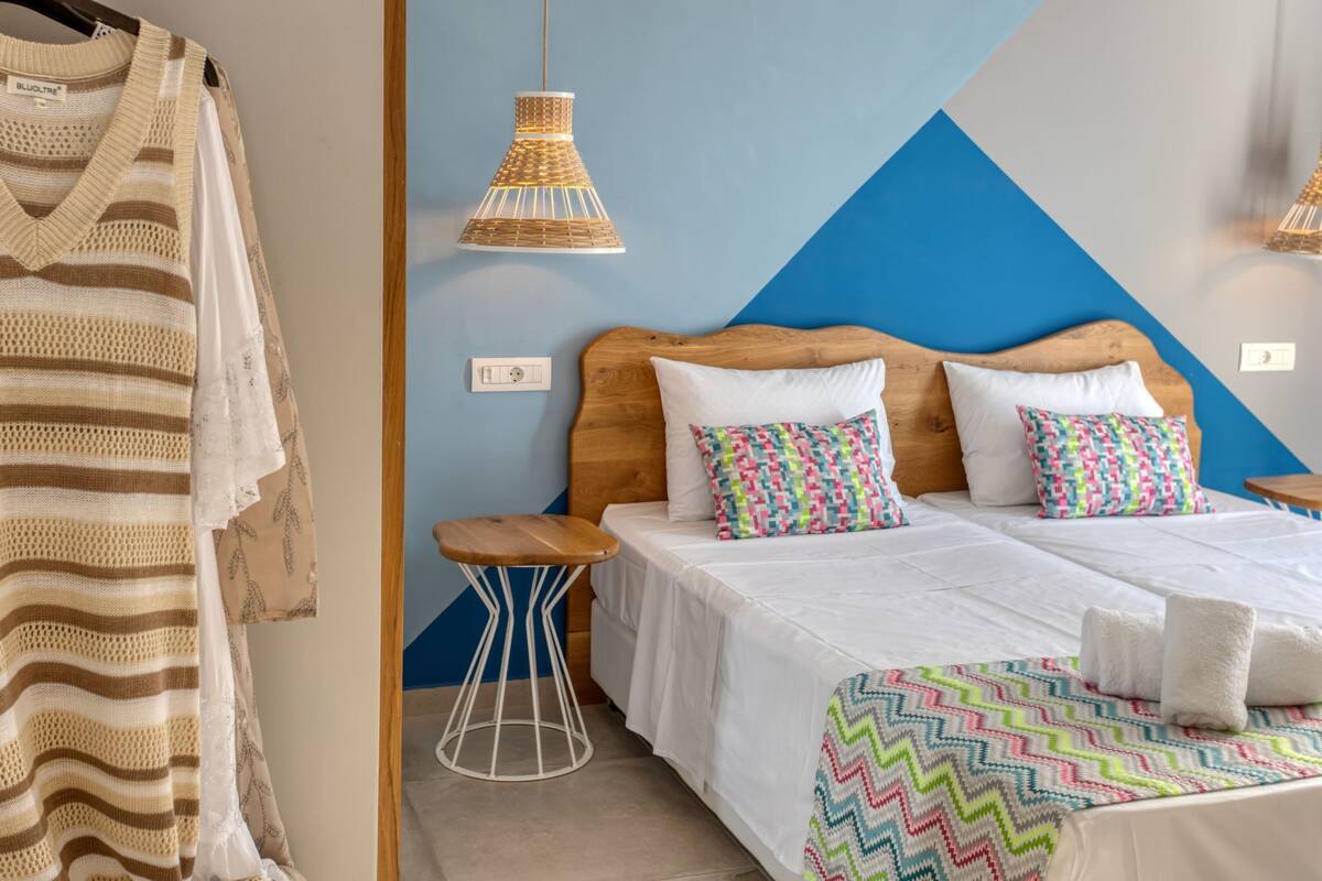 A hotel room with a bed, two pillows, a bedside table, a hanging light, and a wall with a geometric design.