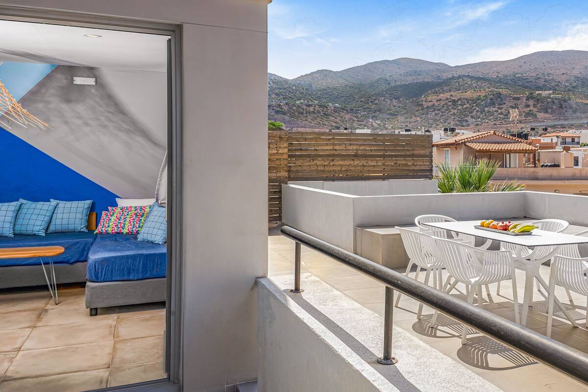 A balcony with a dining area, a sofa with cushions, and a view of a mountainous landscape.
