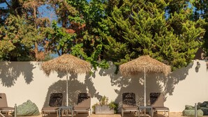 Zona de piscina con sillones reclinables, una sombrilla de paja y una pared cubierta de vegetación.