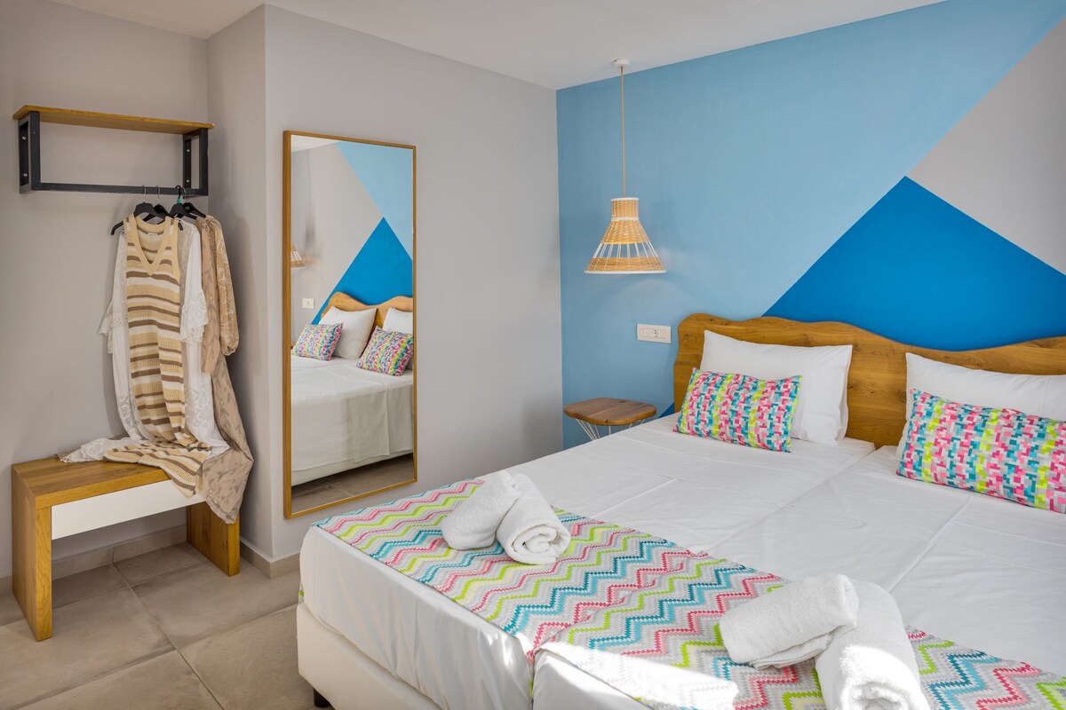Una habitación de hotel con una cama, un banco, un espejo y una lámpara colgante.
